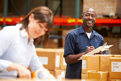 Young man standing next to shipping boxes with clipboard smiling at the camera