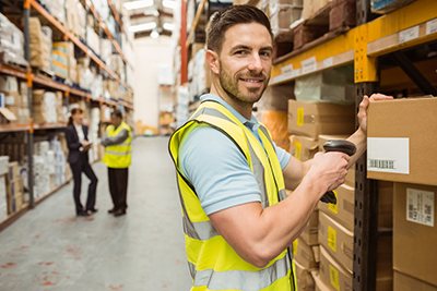 young man wearing a safety vest scanning a package on warehouse shelf