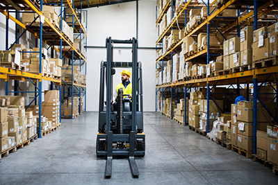 Man wearing a hard hat driving a forklift in warehouse